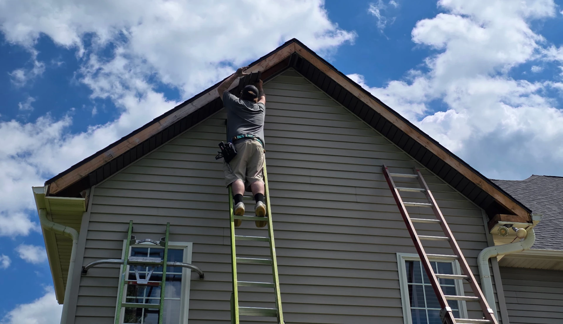 A person on a ladder working on the peak of a house roof, installing soffit and fascia